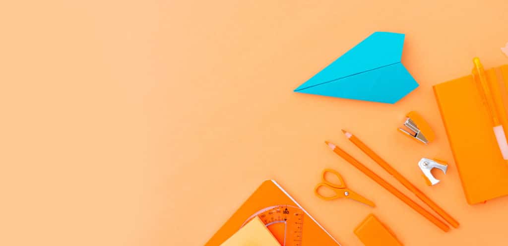 orange background with orange office supplies and turquoise paper airplane