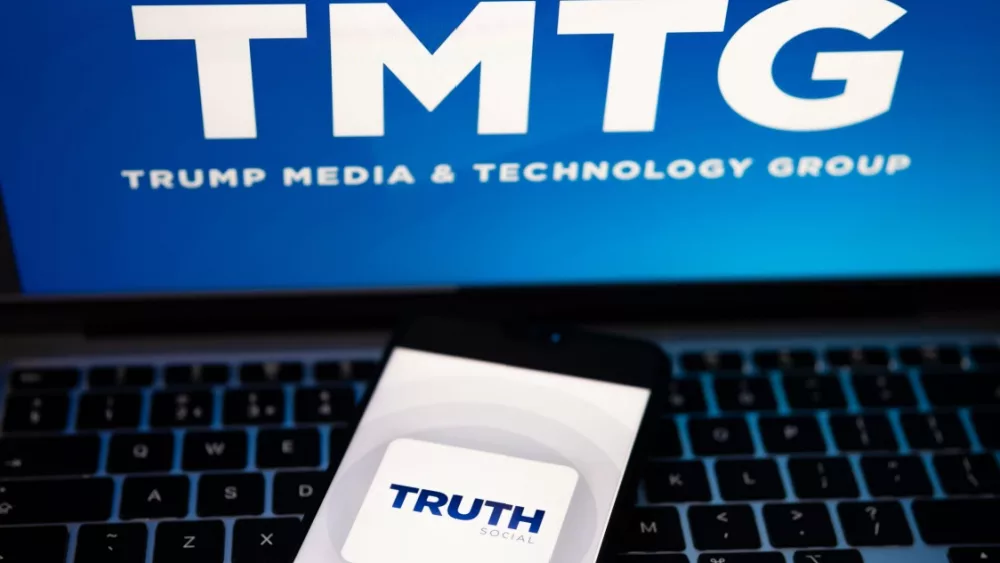 Truth Social app logo seen on the smartphone and blurred TMTG logo on the laptop.