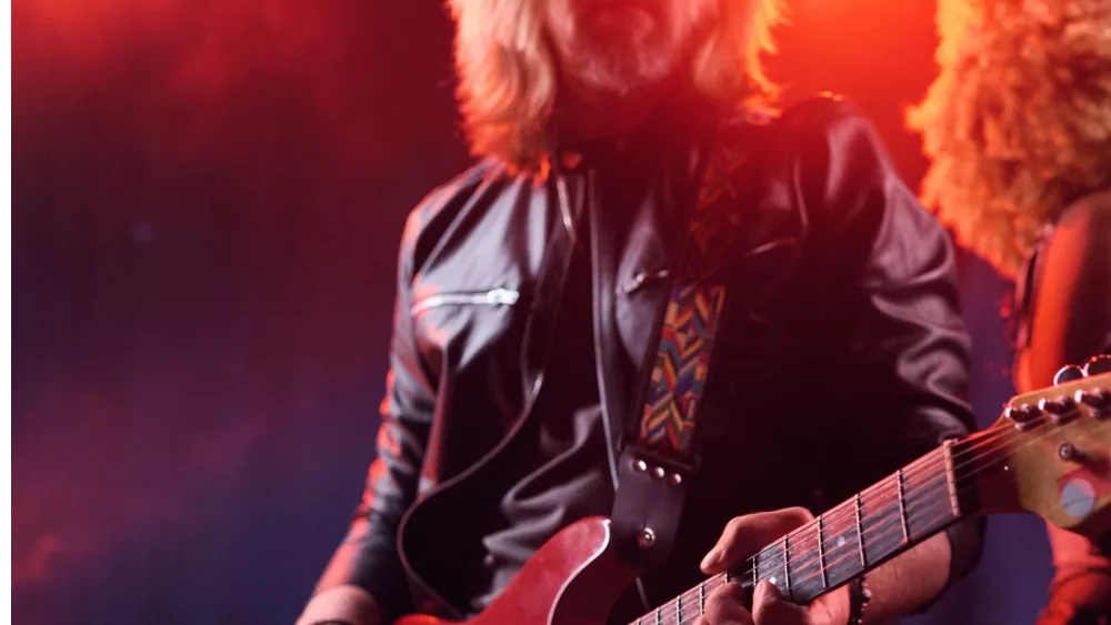 Close up of rock band performing on stage with long haired man playing electric guitar copy space