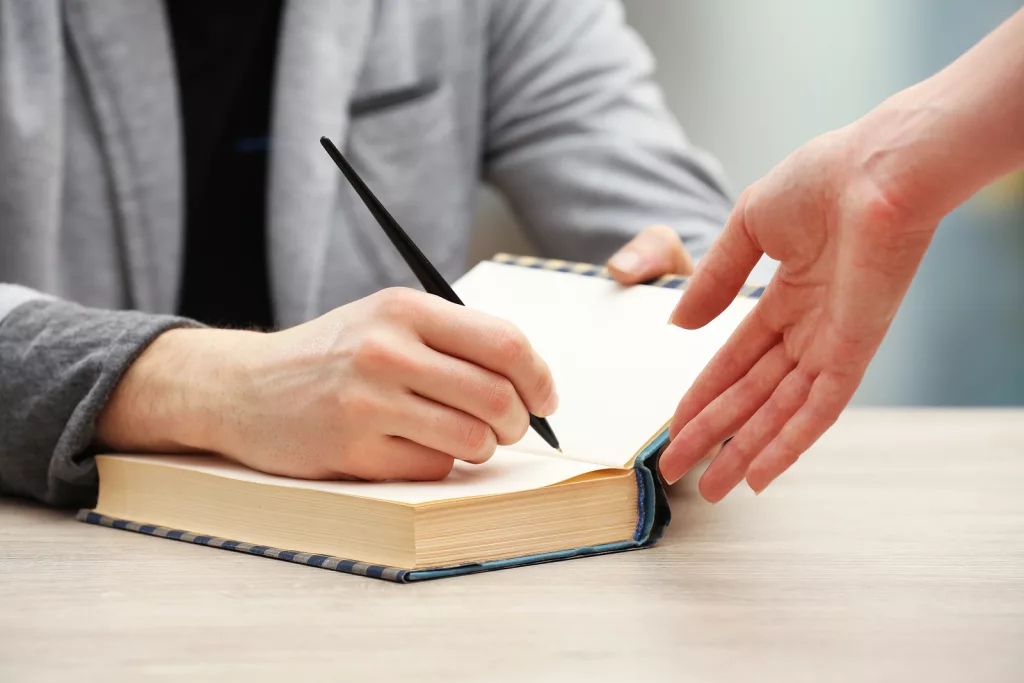 author-signing-autograph-in-own-book-at-wooden-table-on-light-bl