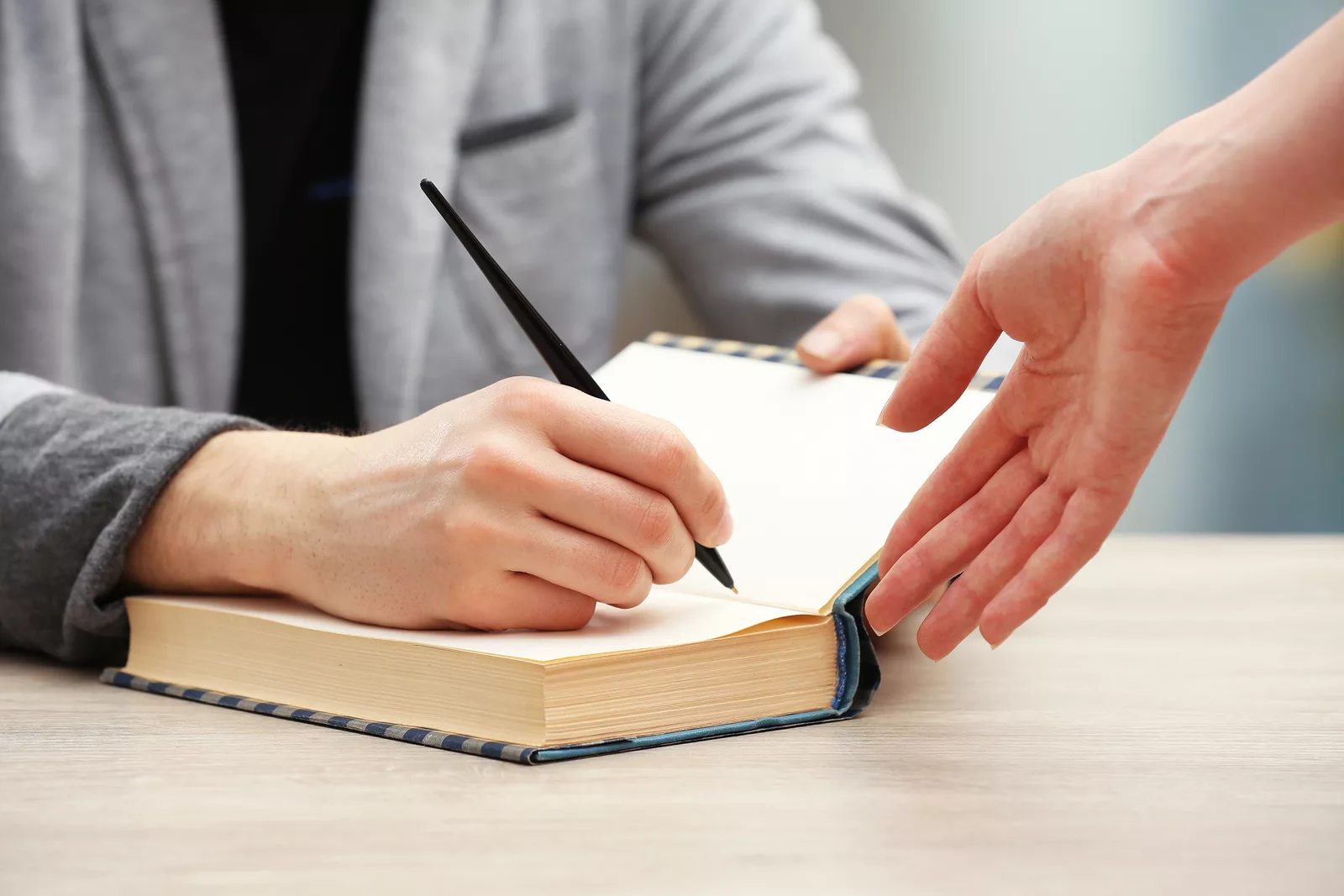 author-signing-autograph-in-own-book-at-wooden-table-on-light-bl