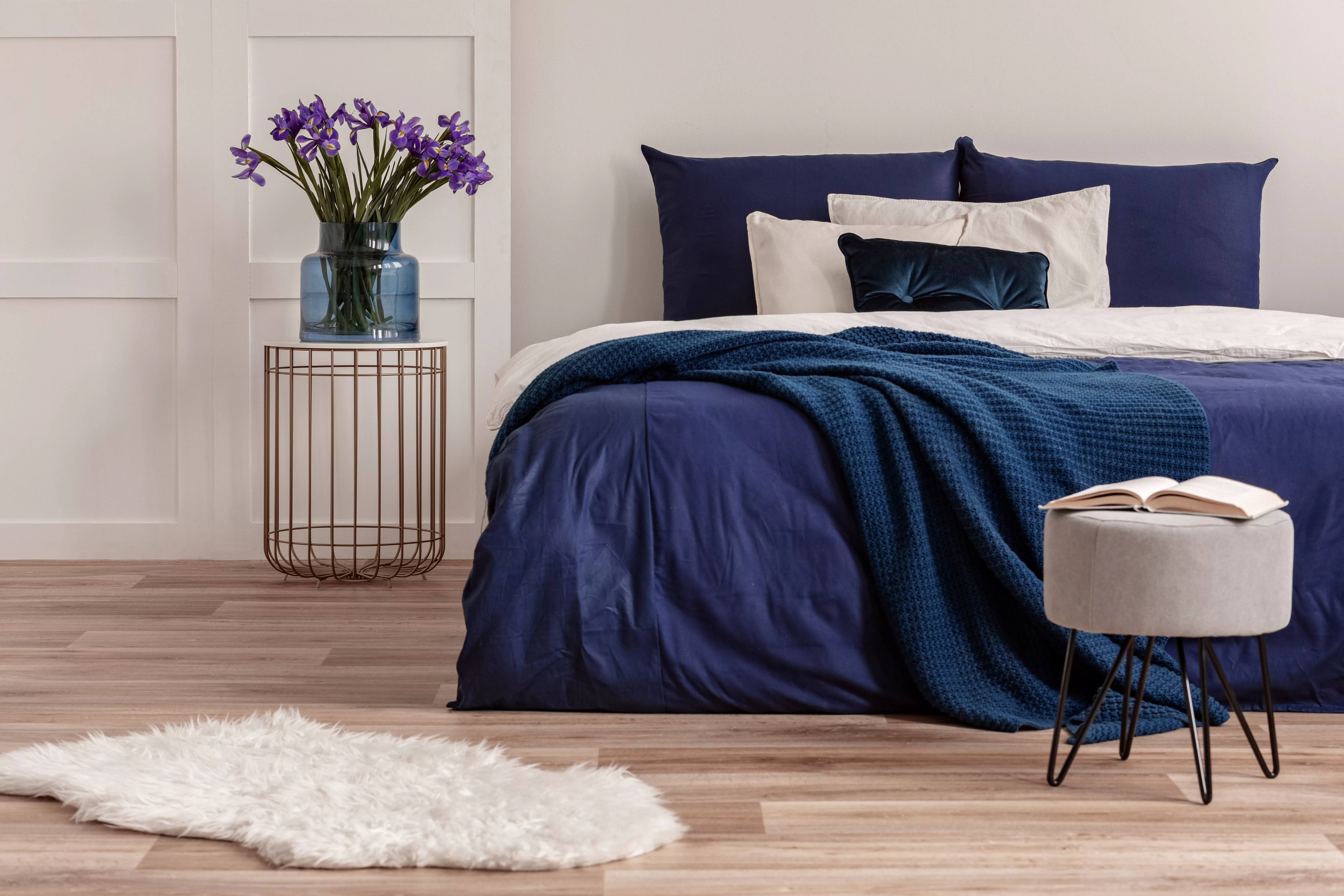 purple-flowers-in-blue-glass-vase-on-stylish-bedside-table-next-to-king-size-bed
