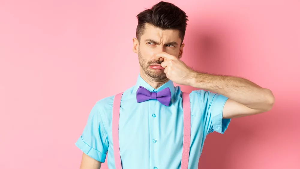 disgusted-young-man-in-bow-tie-and-suspenders-shut-his-nose-from-awful-smell-looking-at-smelly-thing-standing-over-pink-background