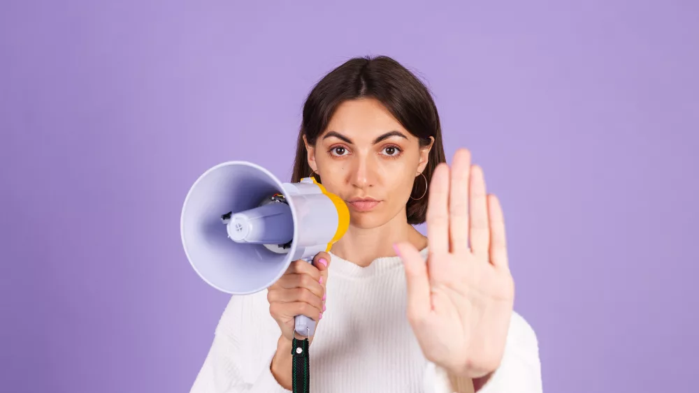 young-brunette-in-white-casual-sweater-isolated-on-purple-background-unhappy-serious-with-megaphone-doing-stop-sing-with-palm-of-the-hand-warning-expression