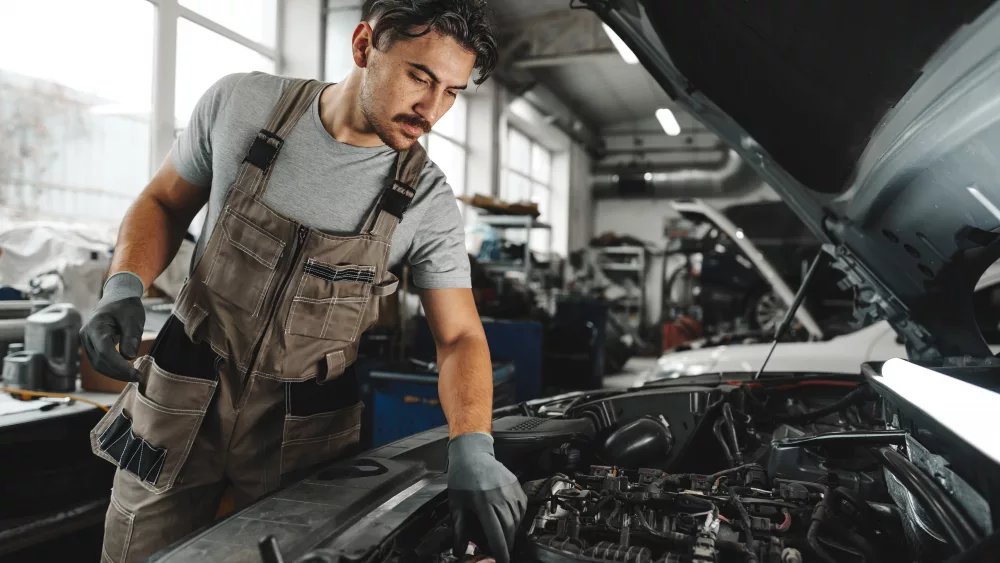 young-male-mechanic-examining-engine-under-hood-of-car-at-the-repair-garage