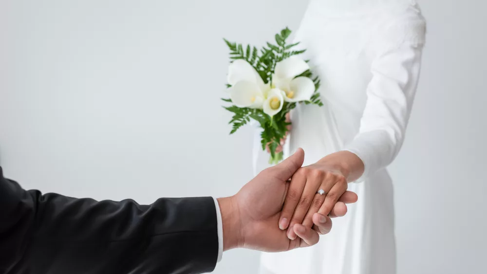 cropped-view-of-bride-with-bouquet-holding-hands-with-blurred-groom-isolated-on-grey