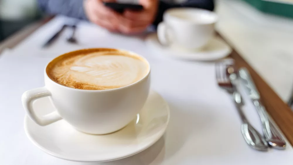cup-with-coffee-on-the-table-in-a-coffee-shop-man-using-a-phone-on-the-background