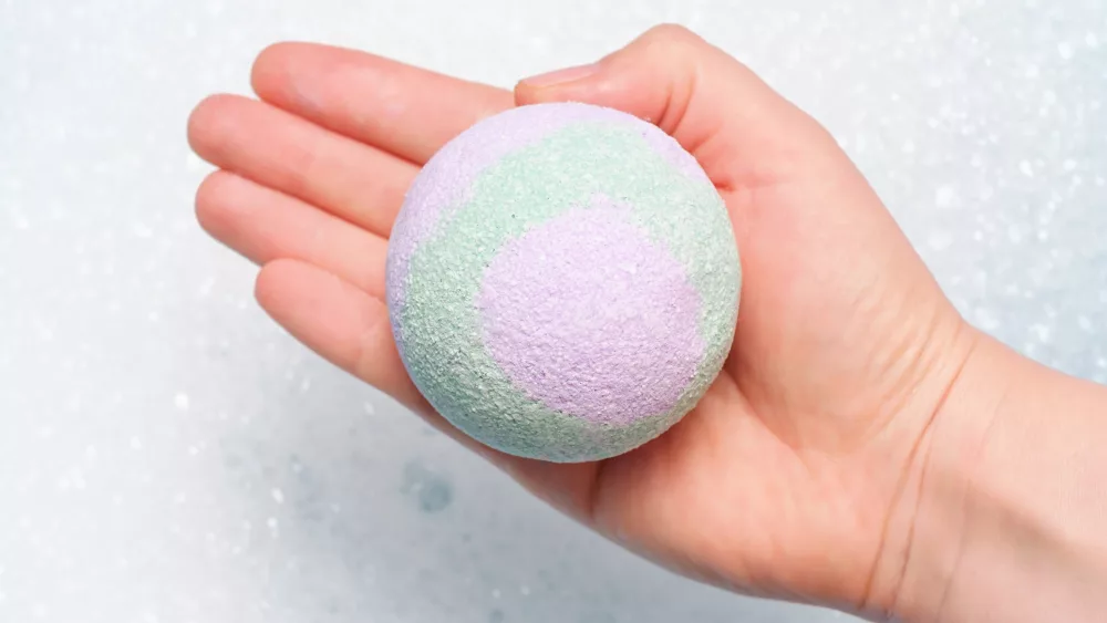 hand-hold-a-bath-bomb-against-the-background-of-foam-close-up