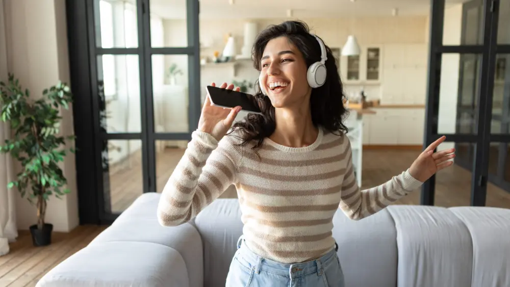 pretty-caucasian-woman-in-wireless-headphones-using-new-music-application-on-smartphone-singing-popular-songs-at-home
