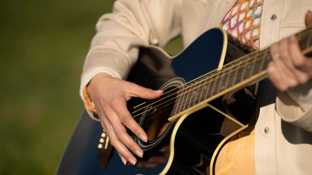 female-hands-delicately-strumming-acoustic-guitar-strings-amid-peaceful-natural-landscape-capturing-musical-creativity-and-serene-outdoor-moment