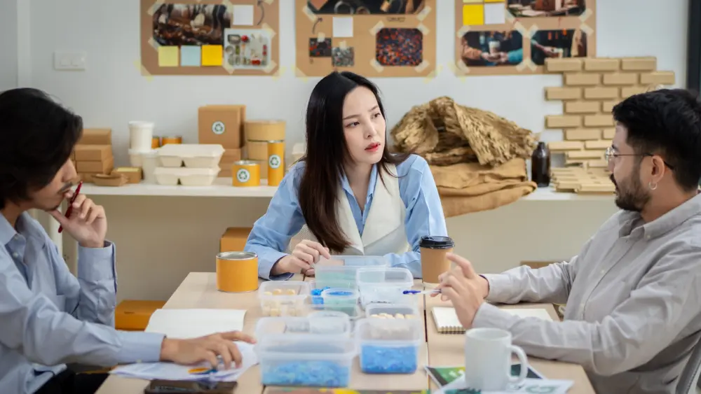 three-people-are-sitting-at-a-table-in-a-room-with-a-whiteboard