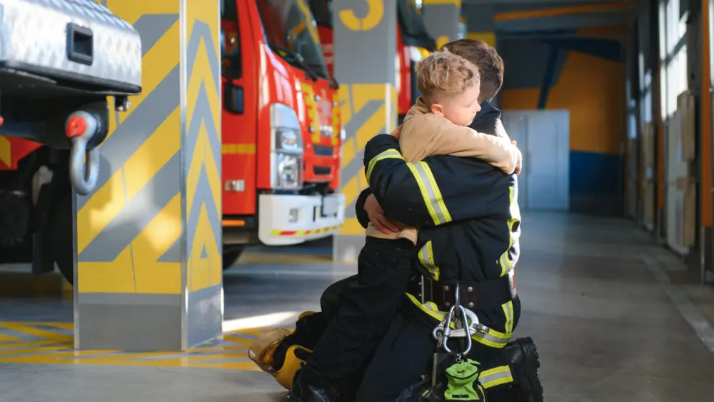 a-firefighter-take-a-little-child-boy-to-save-him-fire-engine-car-on-background
