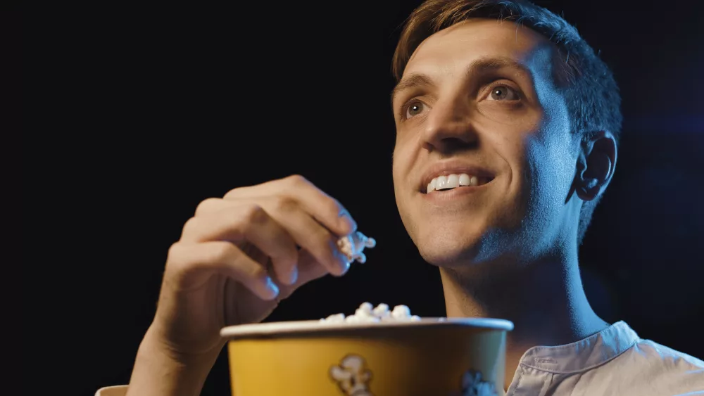 smiling-man-watching-a-movie-and-eating-popcorn
