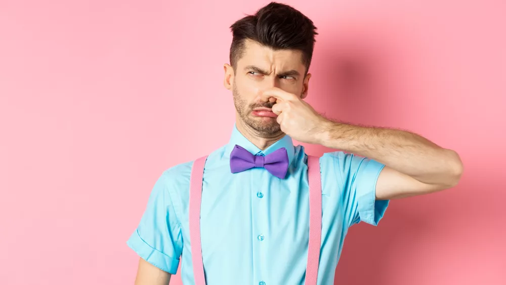 disgusted-young-man-in-bow-tie-and-suspenders-shut-his-nose-from-awful-smell-looking-at-smelly-thing-standing-over-pink-background-2