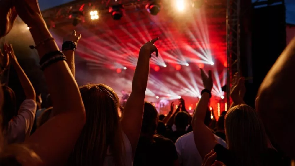 Silhouettes of crowd at concert in front of stage with bright spotlights. People enjoy live music at the band's performance. Concert hall with musicians on stage and fans during music festival