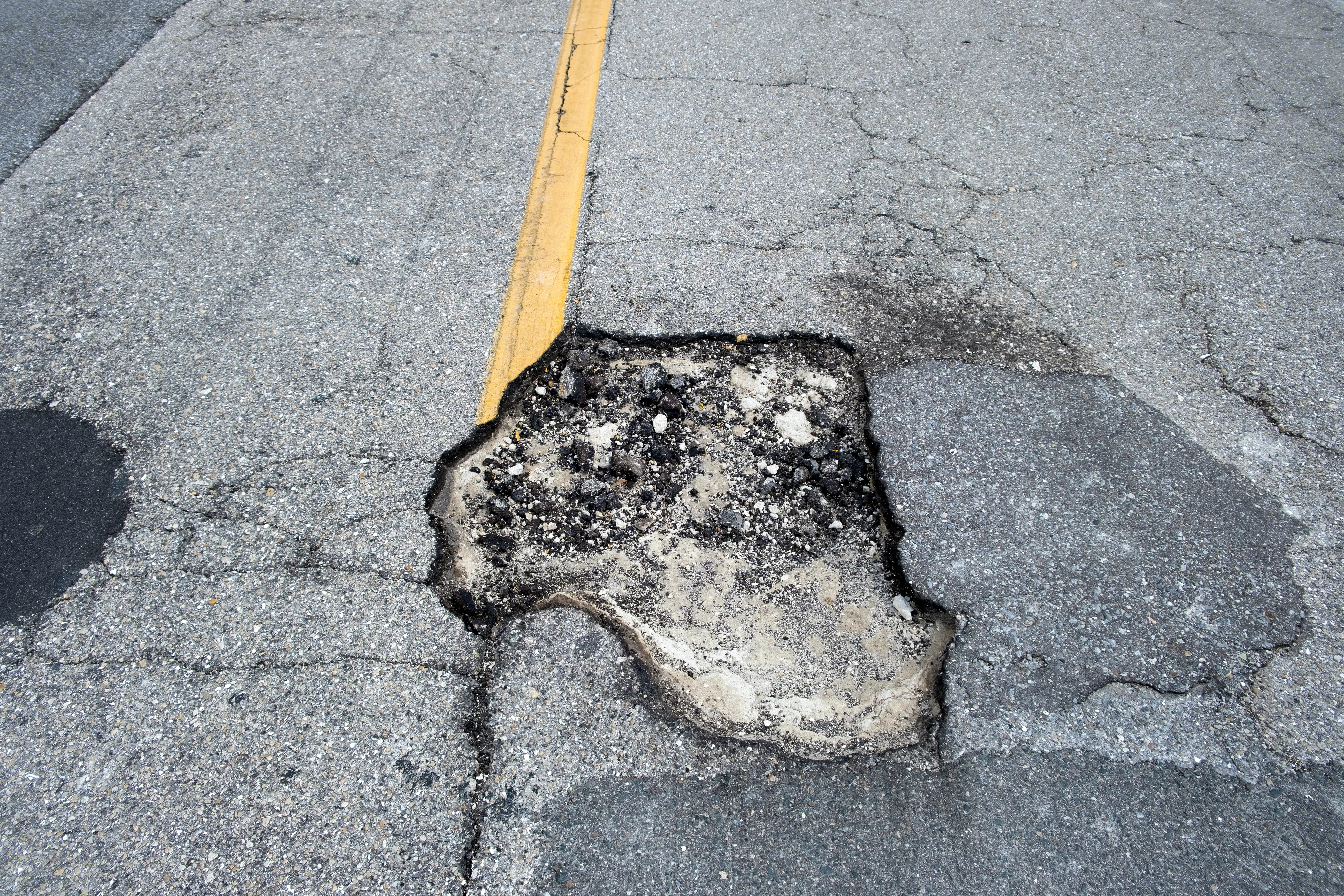 Damaged asphalt road with deep pothole on american highway surface. Ruined roadway in urgent need of repair.