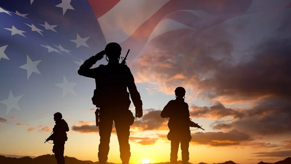 silhouettesofasoldierswithusaflagagainstthesunset