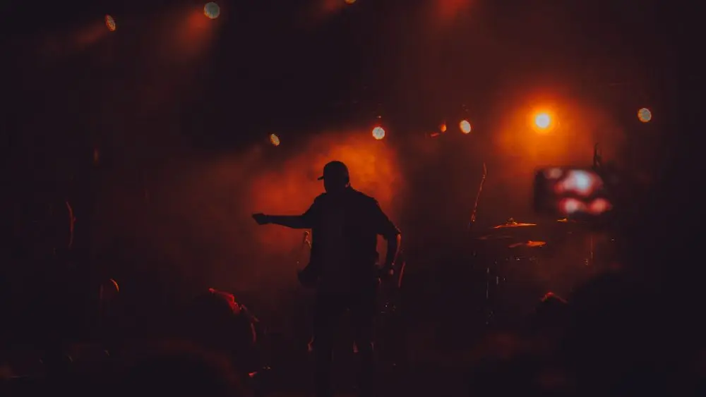 rap singer on stage/ cellphone lighting shown^ dark ambiance
