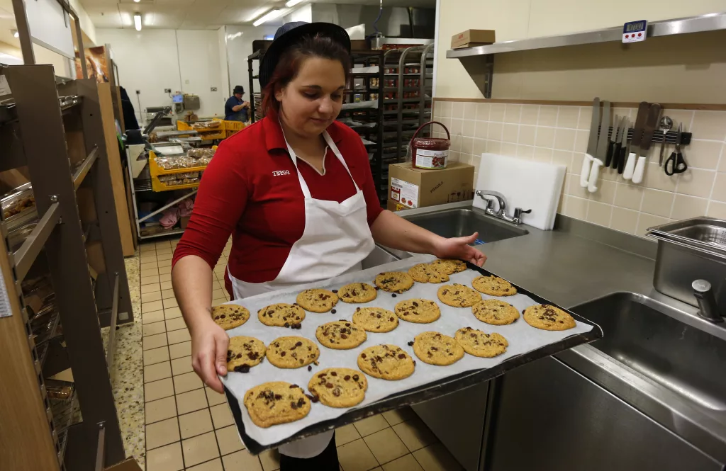 tesco-employee-francis-carries-a-tray-of-chocolate-chip-cookies-in-the-bakery-at-a-tesco-shop-in-bishops-stortford-southern-england