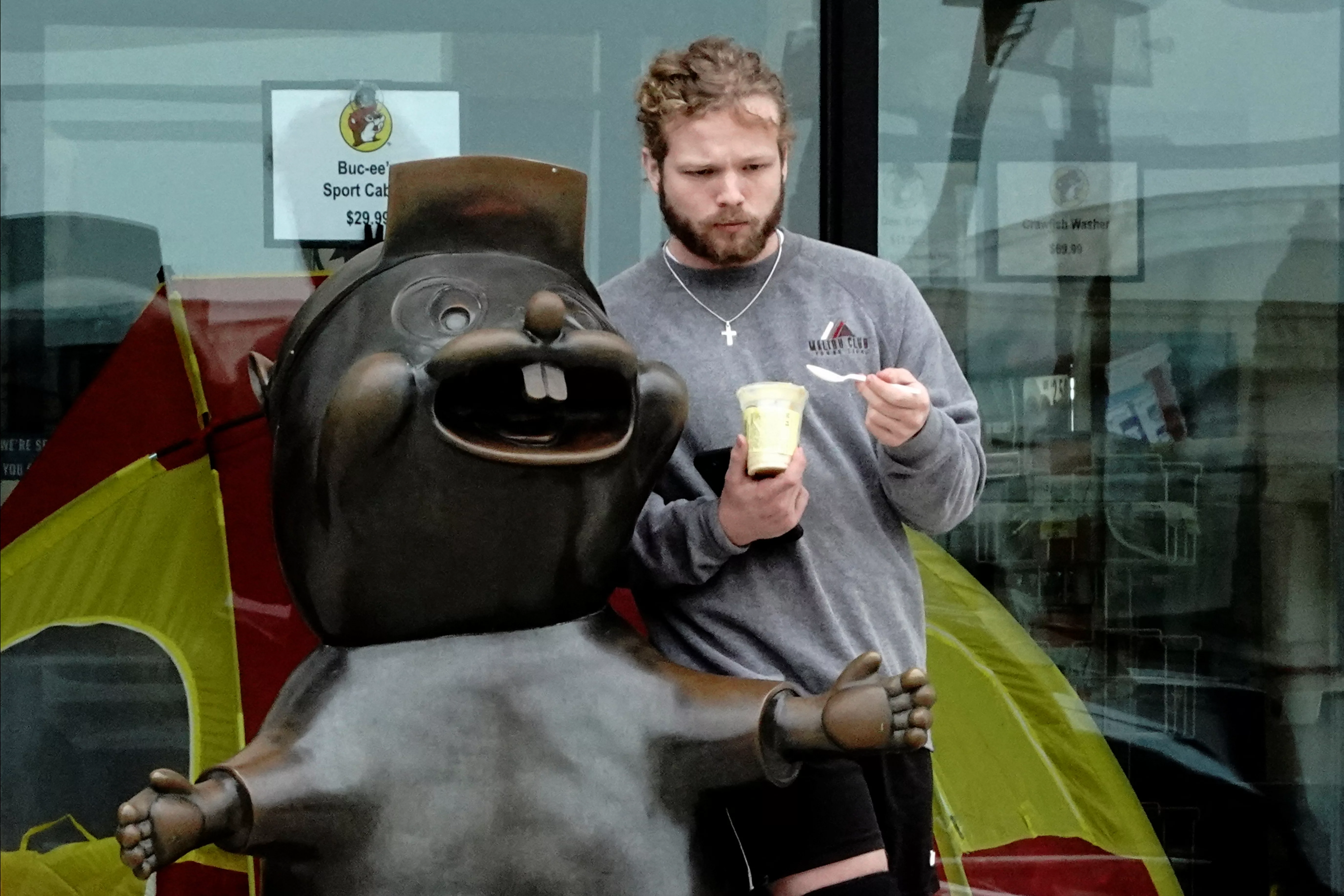 a-man-eats-a-frozen-treat-next-to-a-statue-of-bucc-ee-the-beaver-mascot-of-the-buc-ees-chain-of-gas-stations-and-travel-centers-in-baytown