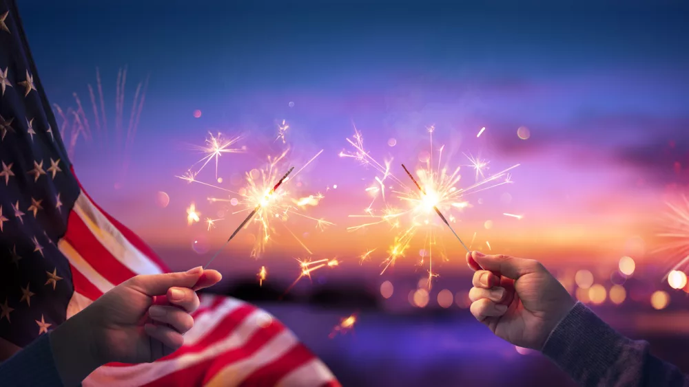 usa-celebration-with-hands-holding-sparklers-and-american-flag-at-sunset-with-fireworks