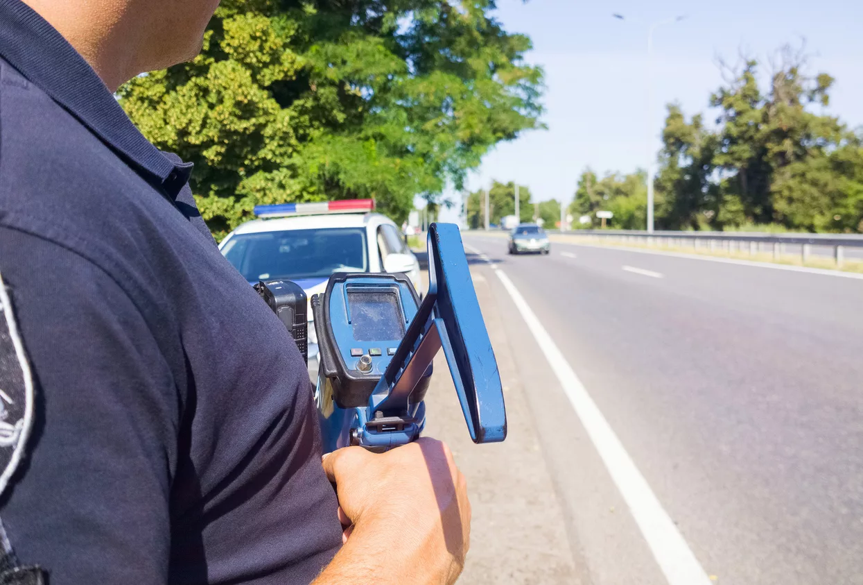 policeman-holding-laser-speed-gun-near-police-car-on-highway-background-selective-focus-part-of-body