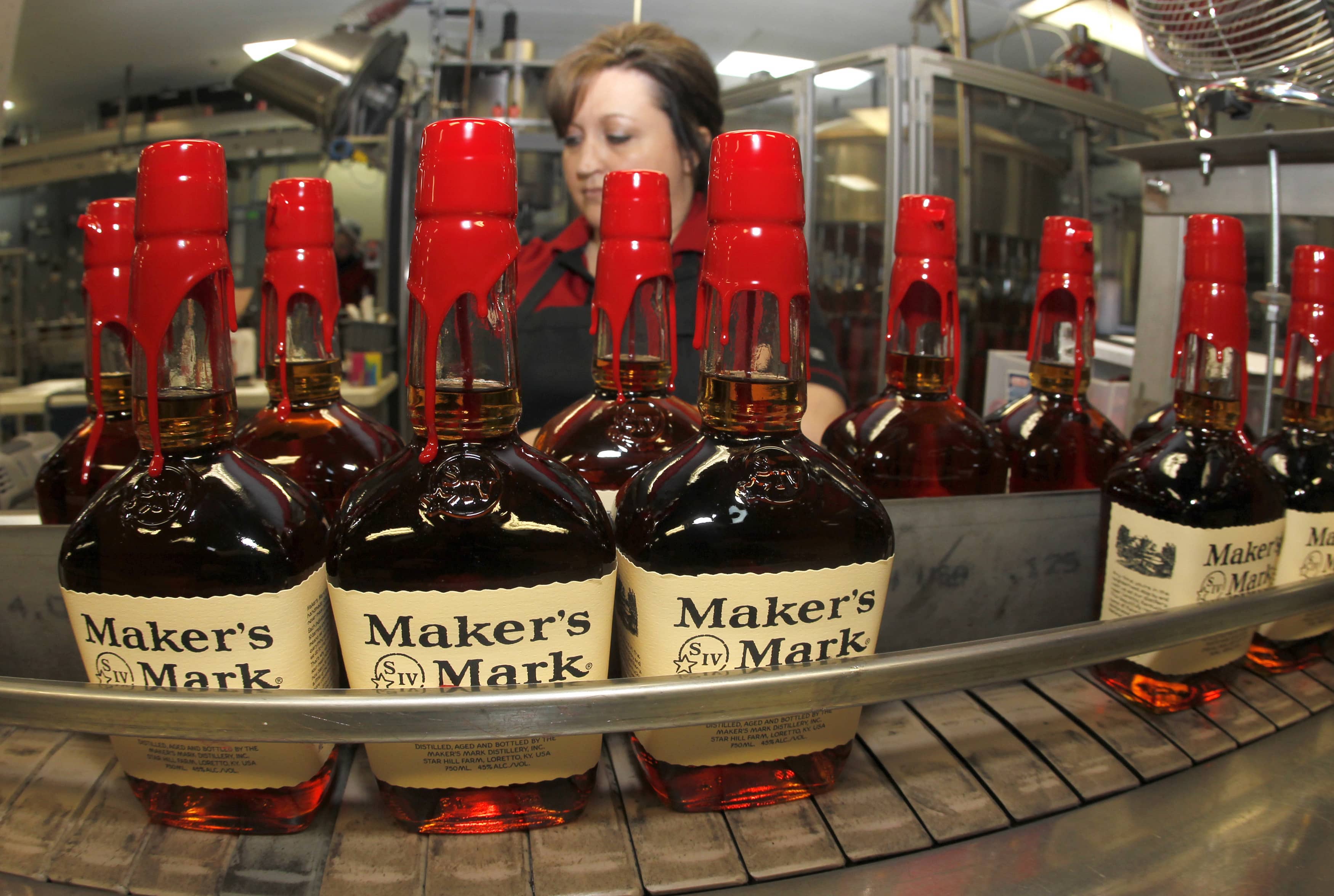 new-bottles-of-makers-mark-bourbon-on-the-conveyor-belt-pass-by-a-worker-after-being-hand-dipped-with-their-signature-red-wax-at-the-makers-mark-distillery-plant-in-loretto