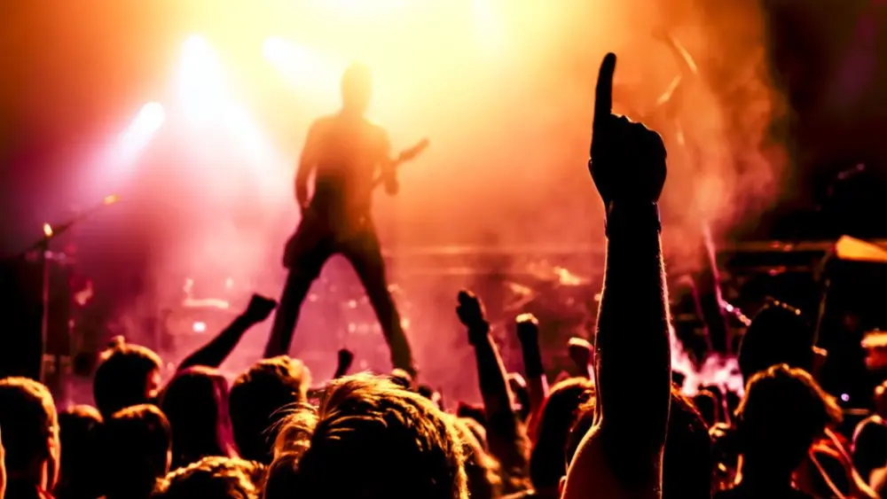 view from crowd cheering rock band performing on stage^ guitarist in silhouette