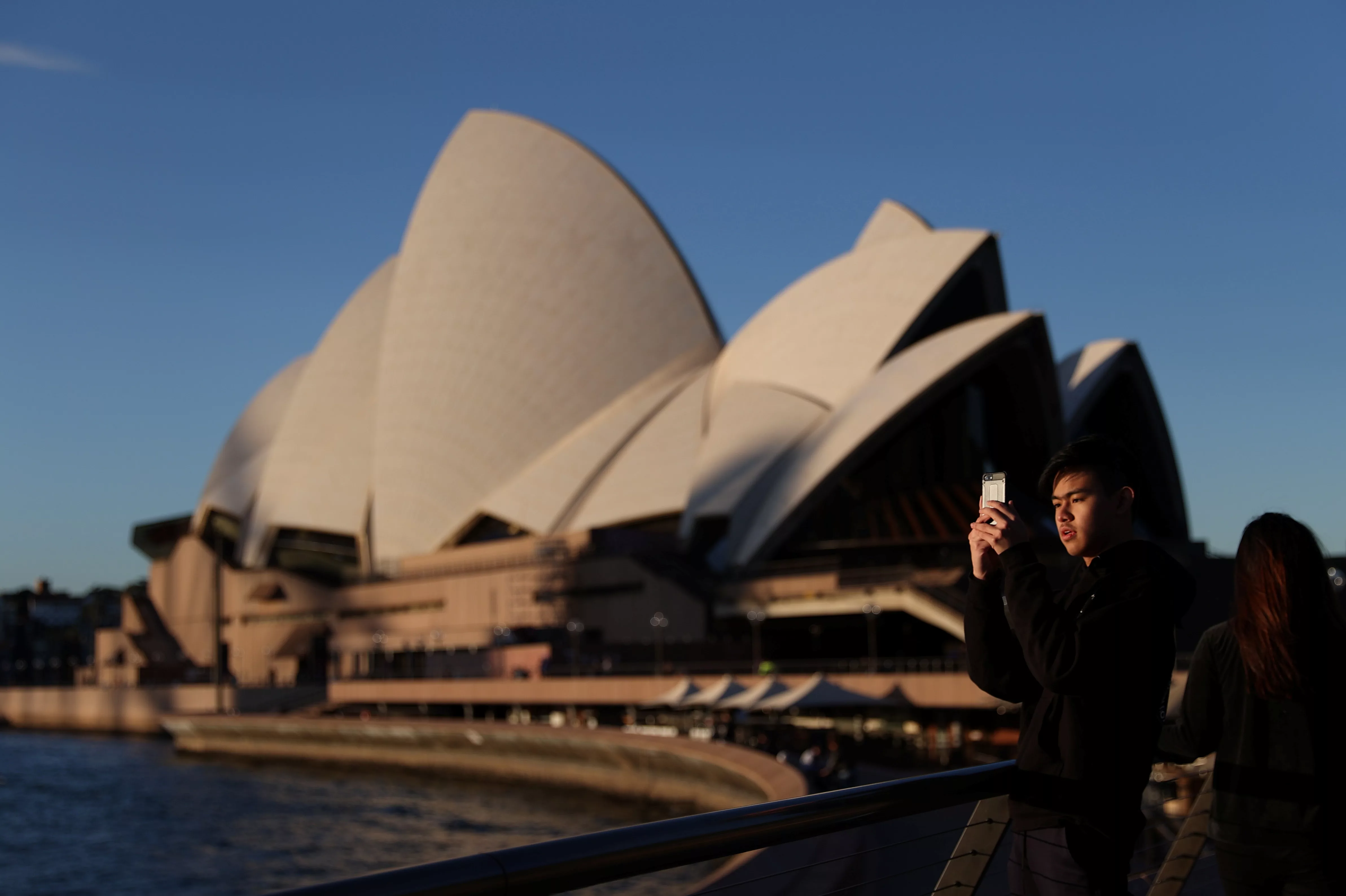 a-young-man-films-with-his-phone-in-front-of-the-sydney-opera-house-in-sydney