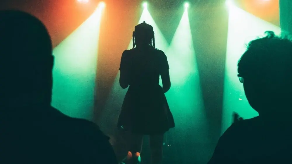 Silhouette of a woman on stage performing with view of people in audience watching^ orange and green spotlights