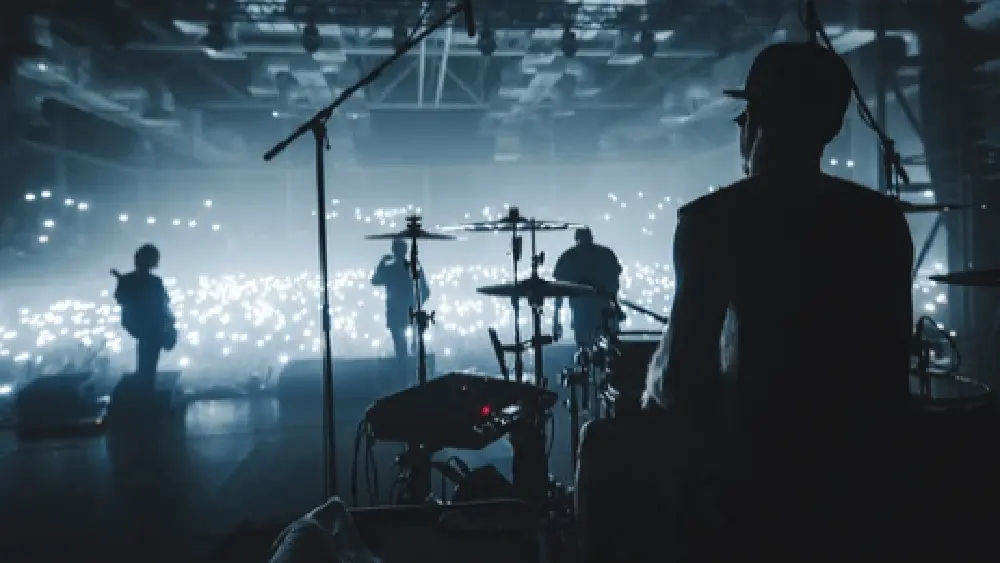 rock band viewed from behind the stage performing to sold-out audience; view of drummers^ guitarists in silhouette in hazy photo