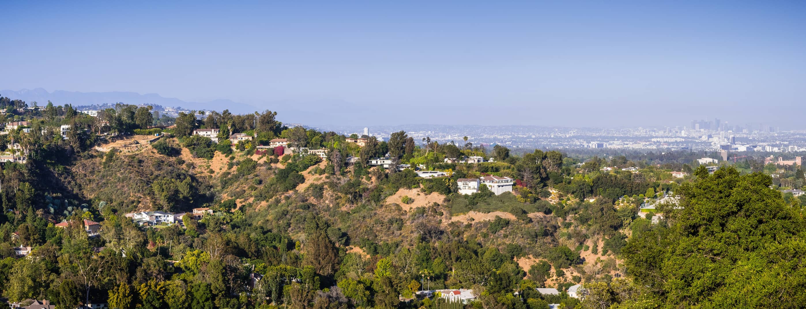 scattered-mansions-on-one-of-the-hills-of-bel-air-neighborhood-the-downtown-skyscrapers-visible-in-the-background-through-a-hazy-atmosphere-los-angeles-california