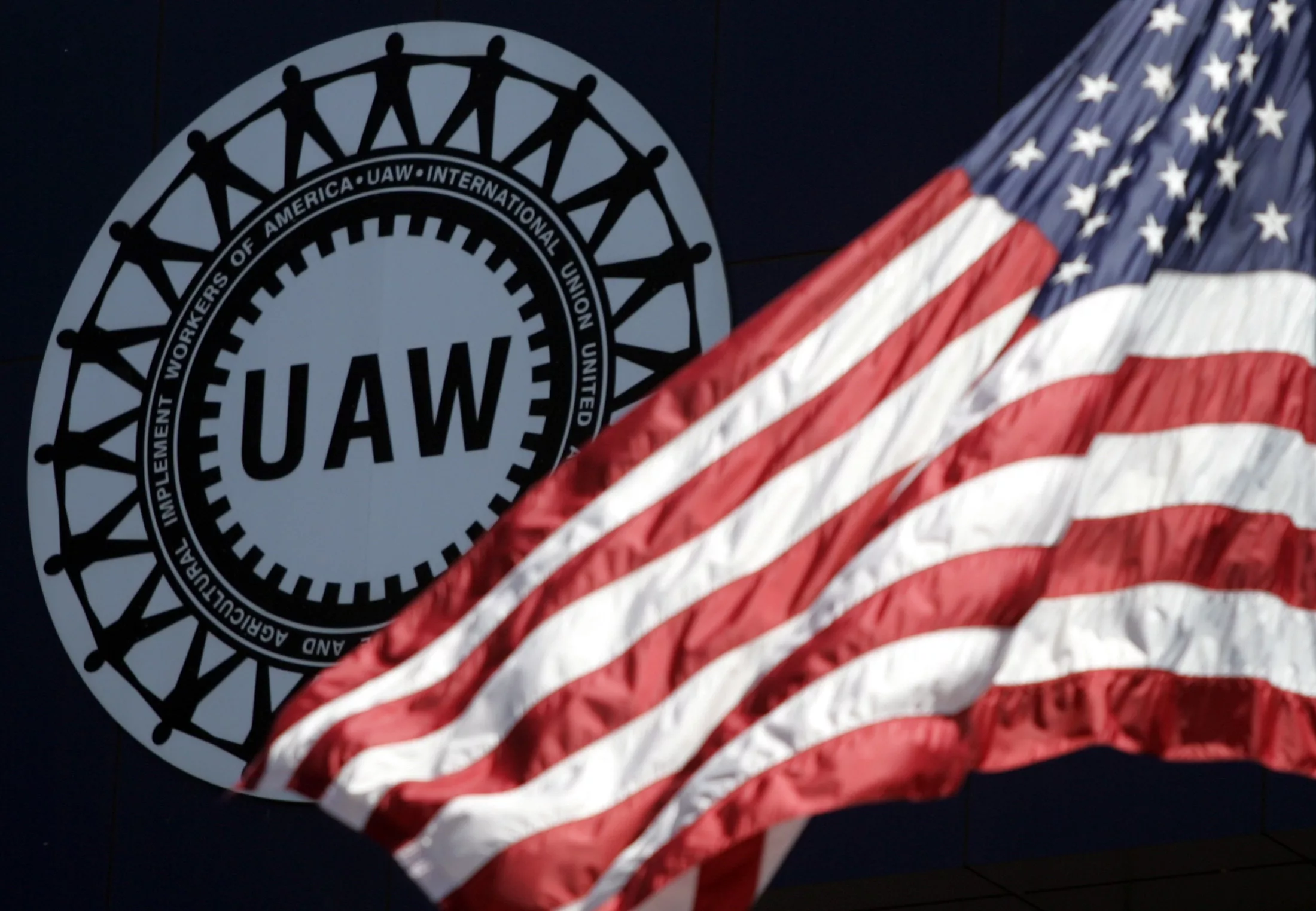 a-u-s-flag-flutters-in-the-wind-in-front-of-the-the-uaw-logo-outside-the-united-auto-workers-union-solidarity-house-in-detroit