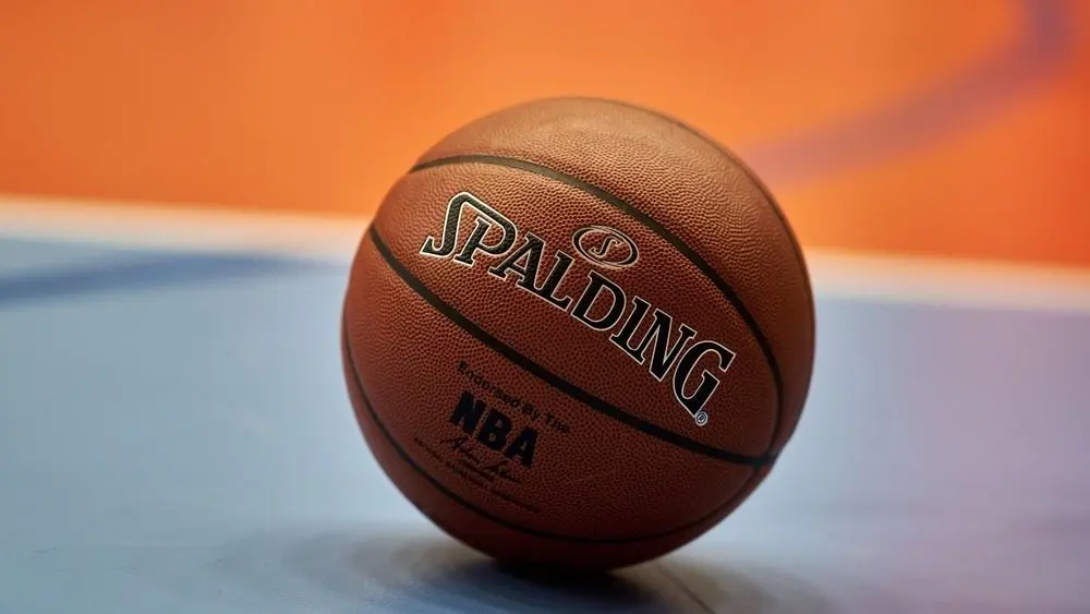 Close-up of a Spalding NBA basketball resting on a blue and orange court^ focusing on the texture of the ball and the surrounding vibrant colors of the court.