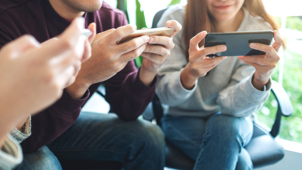 group-of-young-people-using-and-plying-games-on-mobile-phone-while-sitting-together