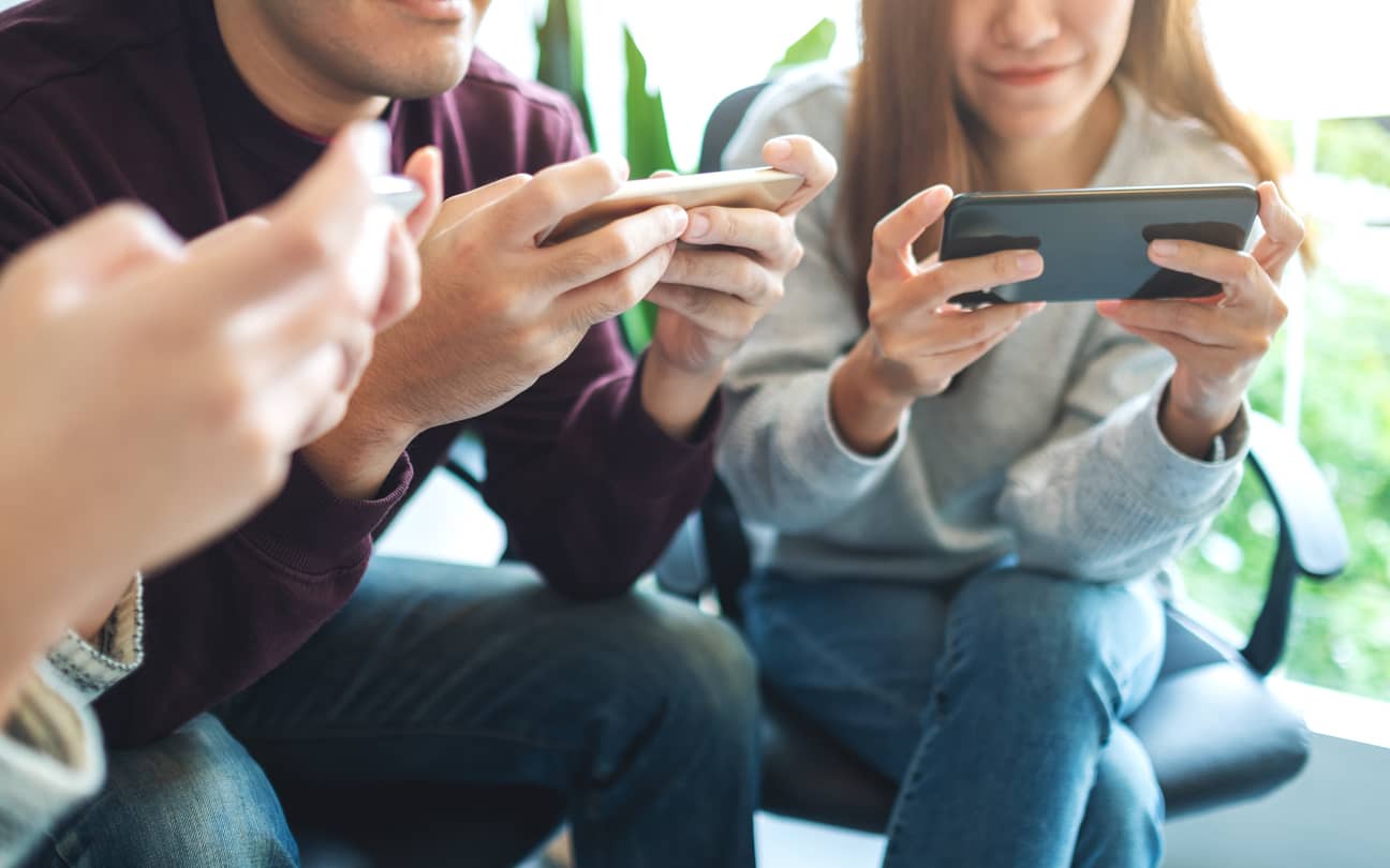 group-of-young-people-using-and-plying-games-on-mobile-phone-while-sitting-together