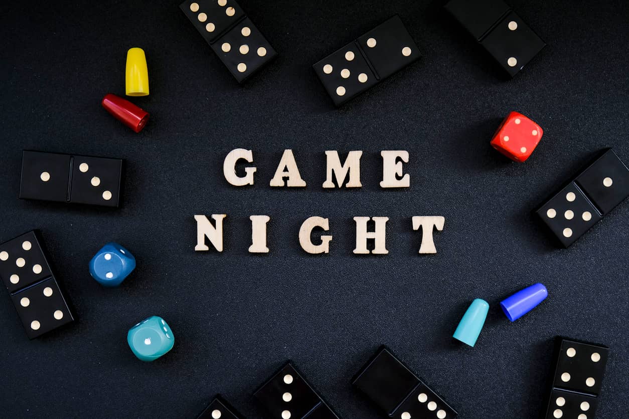 text-game-night-spelled-out-in-wooden-letter-surrounded-by-dice-dominoes-other-game-pieces-on-black-background-table-games-stay-home-activity
