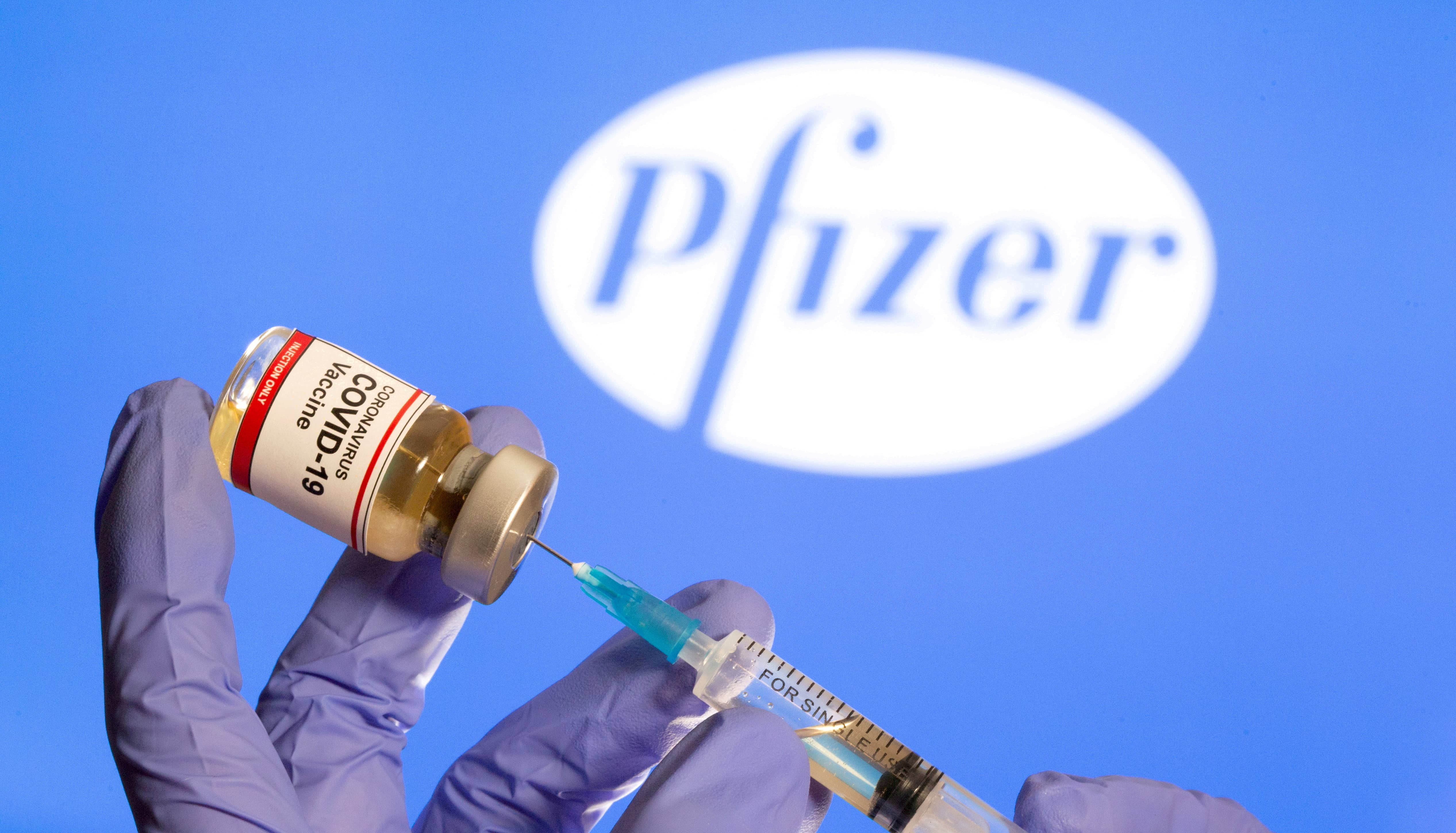 file-photo-file-photo-a-woman-holds-a-small-bottle-labeled-with-a-coronavirus-covid-19-vaccine-sticker-and-a-medical-syringe-in-front-of-displayed-pfizer-logo-in-this-illustration