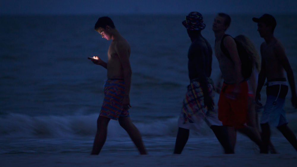 file-photo-of-a-person-looksing-at-cell-phone-as-he-and-others-walk-along-beach-at-twilight-during-labour-day-long-weekend-in-ft-myers-beach-florida