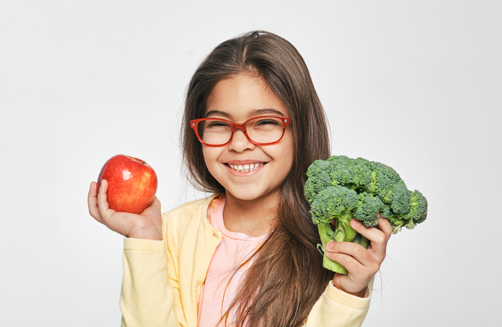 smiling-mixed-race-girl-holding-an-apple-and-broccoli-in-her-hands-healthy-vegetarian-food-for-kids