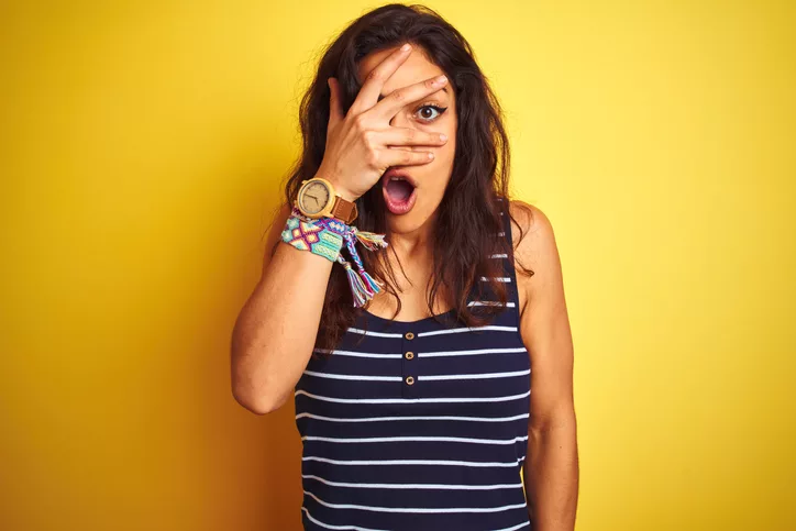 young-beautiful-woman-wearing-striped-t-shirt-standing-over-isolated-yellow-background-peeking-in-shock-covering-face-and-eyes-with-hand-looking-through-fingers-with-embarrassed-expression