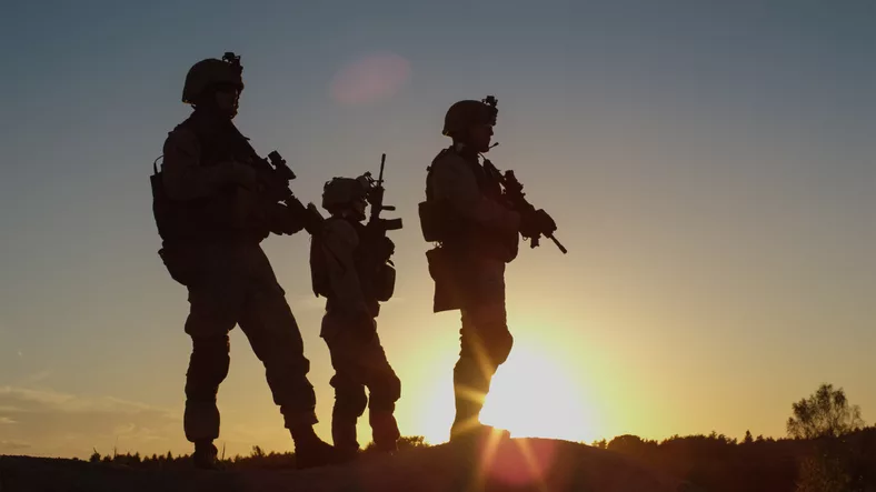 squad-of-three-fully-equipped-and-armed-soldiers-standing-on-hill-in-desert-environment-in-sunset-light