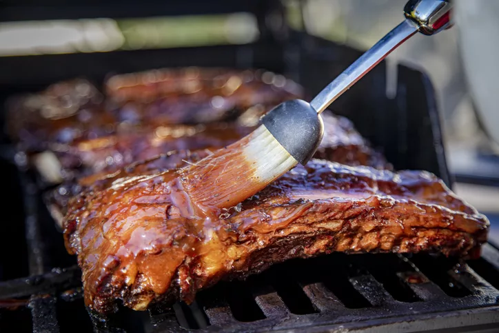 beef-ribs-being-basted-with-bbq-sauce-on-a-grill-with-a-basting-brush