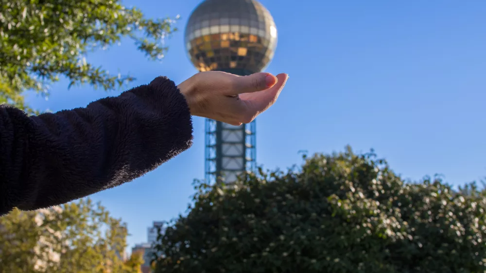 an-illussion-of-a-female-hand-holding-the-golden-globe-of-the-the-sunsphere-tower-in-knoxville-tennessee-usa-with-a-clear-blue-sky-and-greenery-around