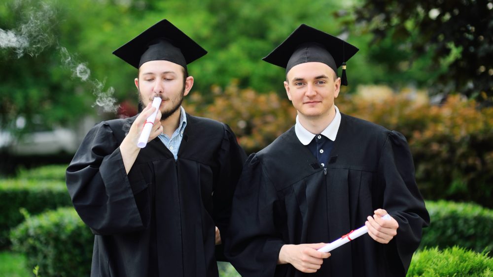 oung-male-graduate-student-in-a-black-robe-and-a-square-hat-smokes-his-diploma-or-certificate-marijuana-cannabis-and-student-life