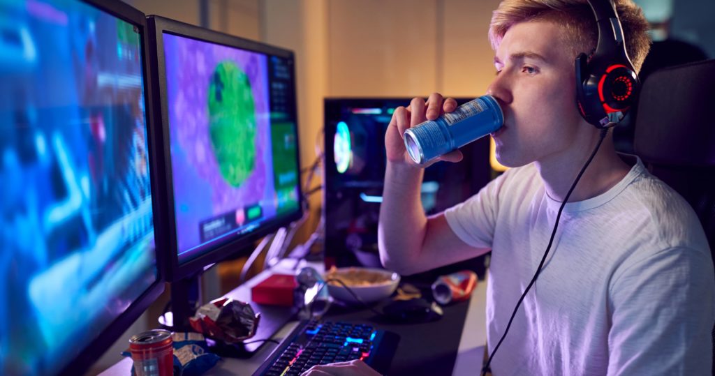 teenage-boy-drinking-caffeine-energy-drink-gaming-at-home-using-dual-computer-screens-at-night