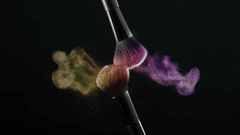 cosmetic-shades-of-different-colors-yellow-and-pink-fly-away-from-two-makeup-brushes-creating-a-fancy-pattern-on-a-black-background