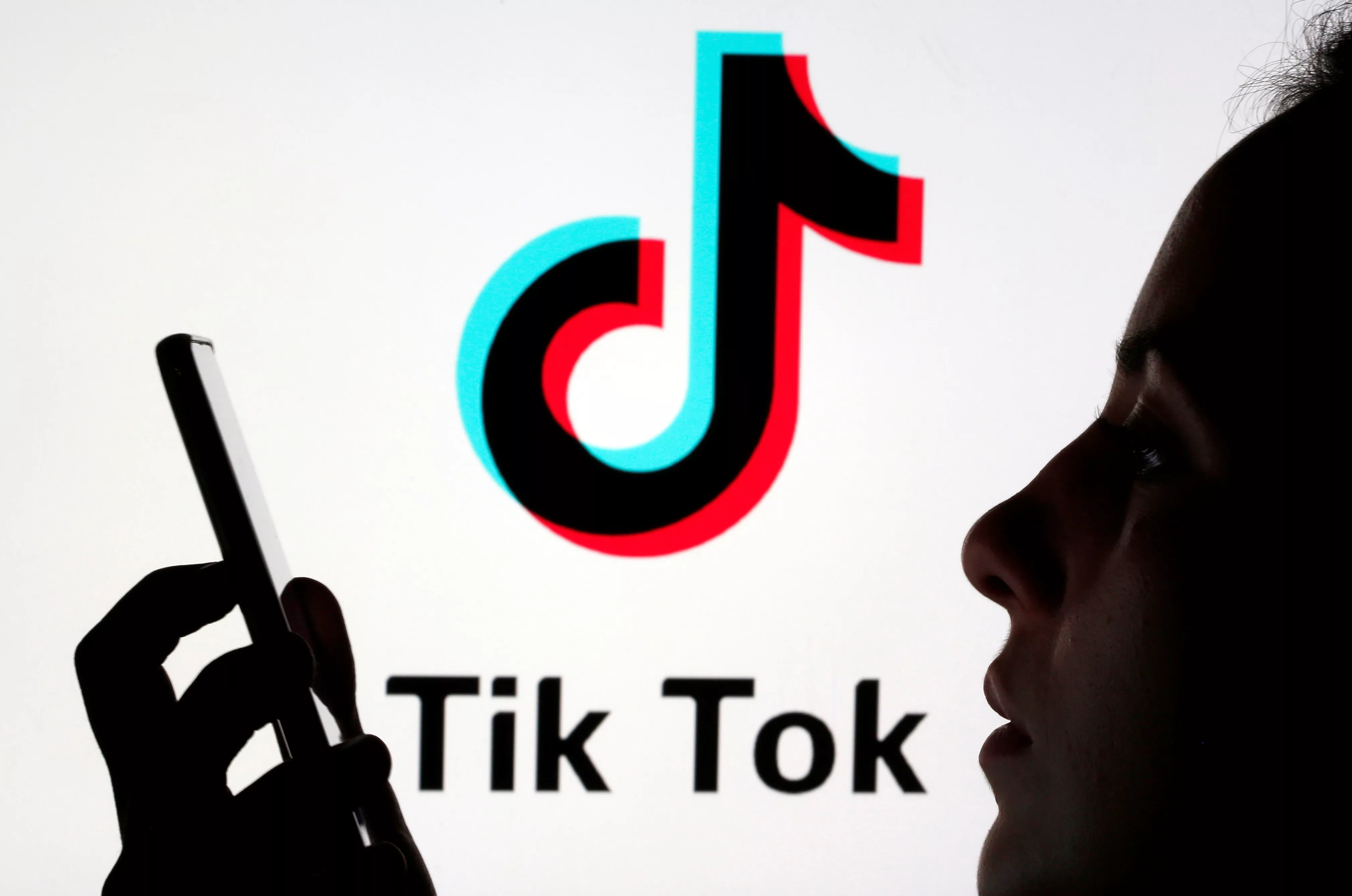 a-person-holds-a-smartphone-as-tik-tok-logo-is-displayed-behind-in-this-picture-illustration