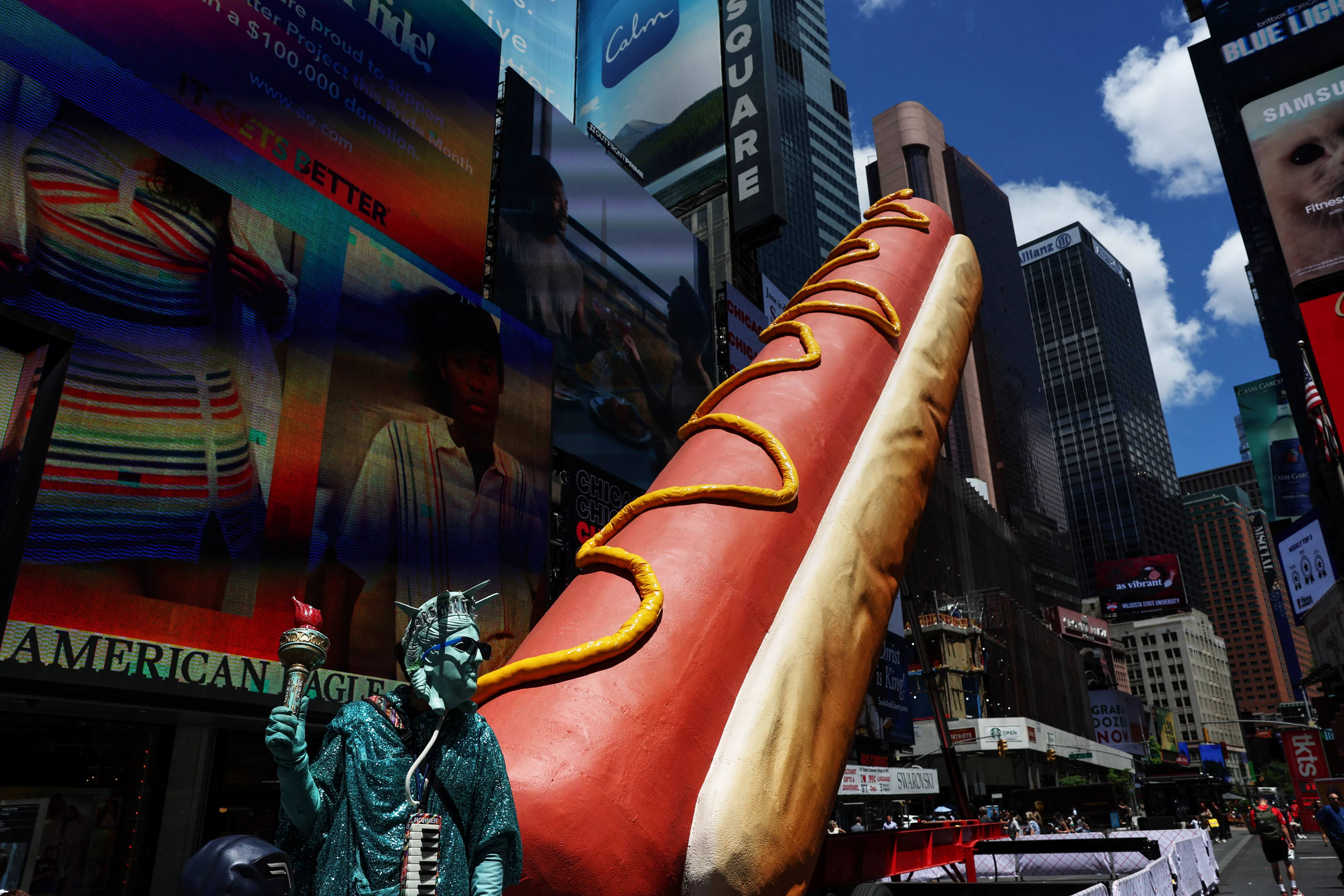 a-man-dressed-as-the-statue-of-liberty-stands-next-a-giant-hot-dog-in-the-times-square-area-in-new-york-city