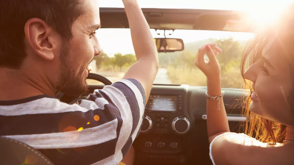 young-couple-driving-along-country-road-in-open-top-car
